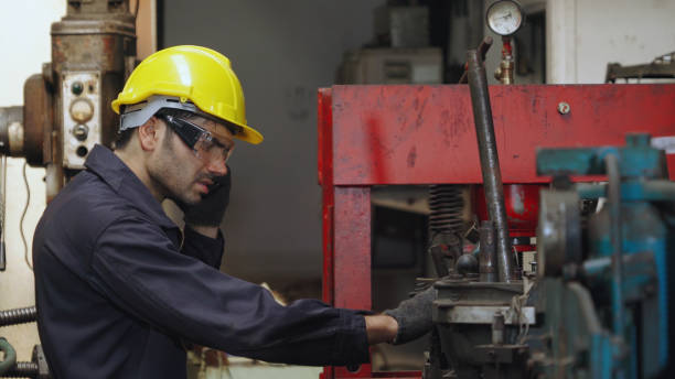 Factory worker talking on portable radio while inspecting machinery parts . Industrial and engineering team communication concept .