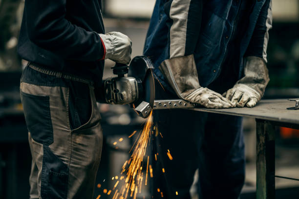 Cropped picture of two metallurgy workers grinding at heavy industry factory.